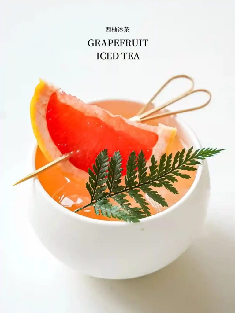 Grapefruit iced tea with a grapefruit slice and fern leaves, served in a white cup.