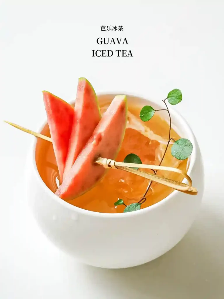 Guava iced tea with fresh watermelon pieces and green leaves, served in a white cup.