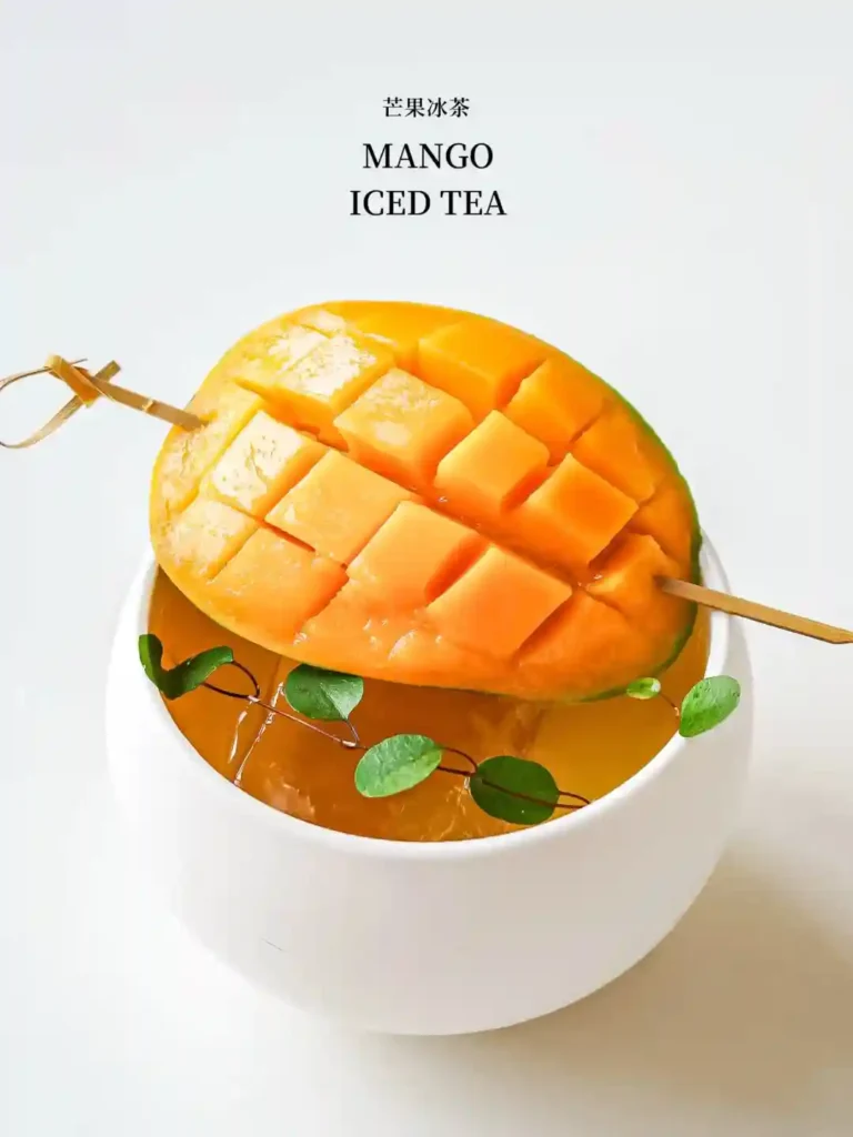 Mango iced tea with cubed mango on top, served in a white cup.