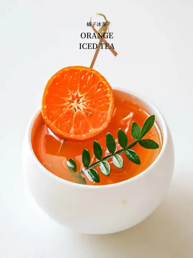 Orange iced tea with a large orange slice and green leaves, served in a white cup.